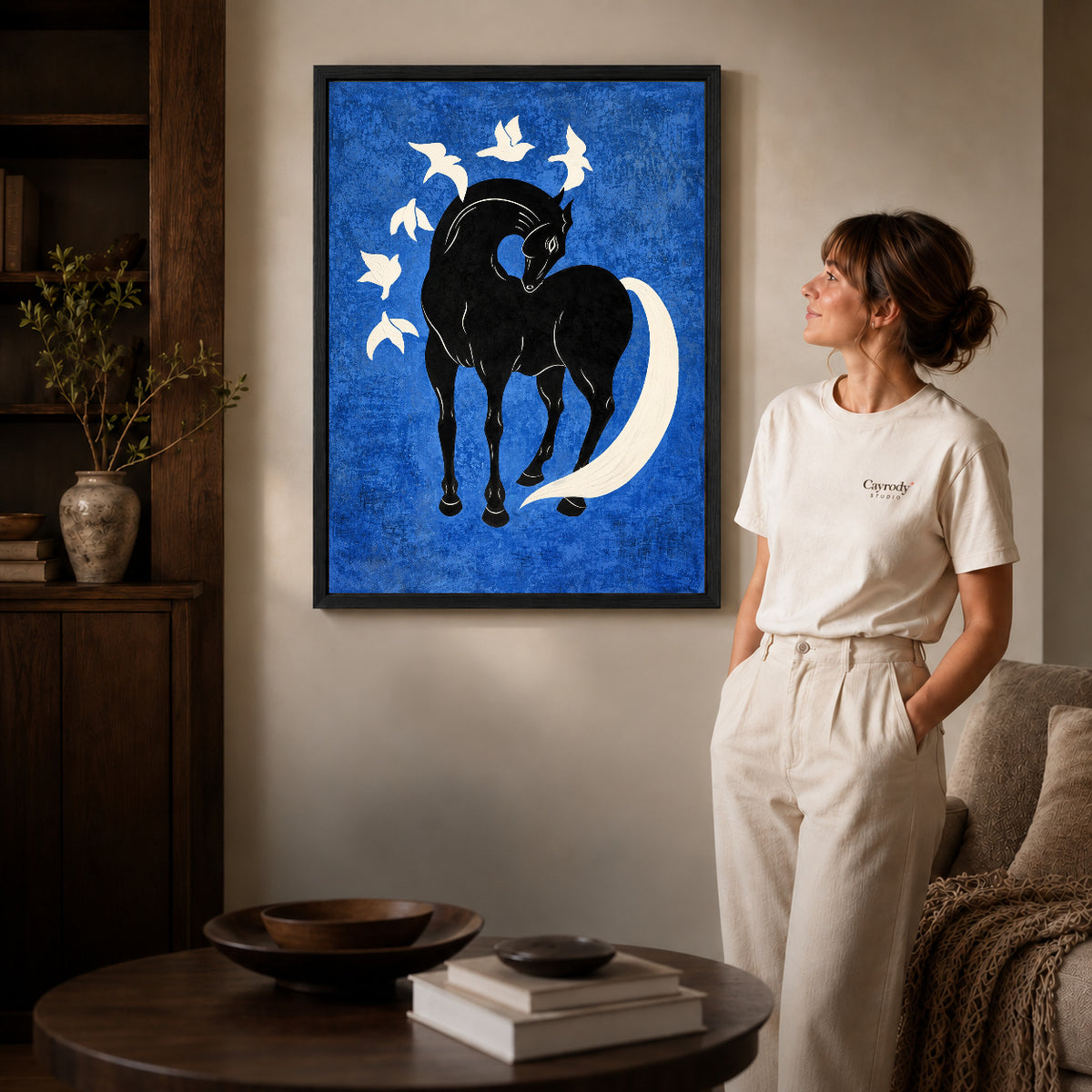 horse bird harmony canvas art in a black frame beside a woman and round wooden table.