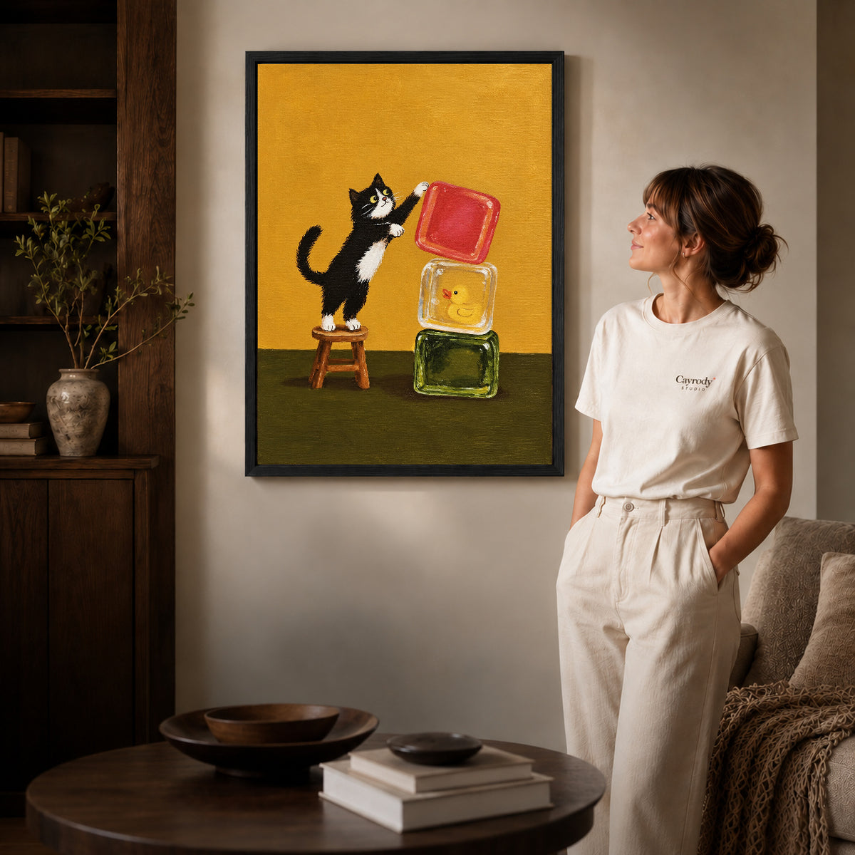 cat block balance canvas art in a black frame beside a woman and round wooden table.
