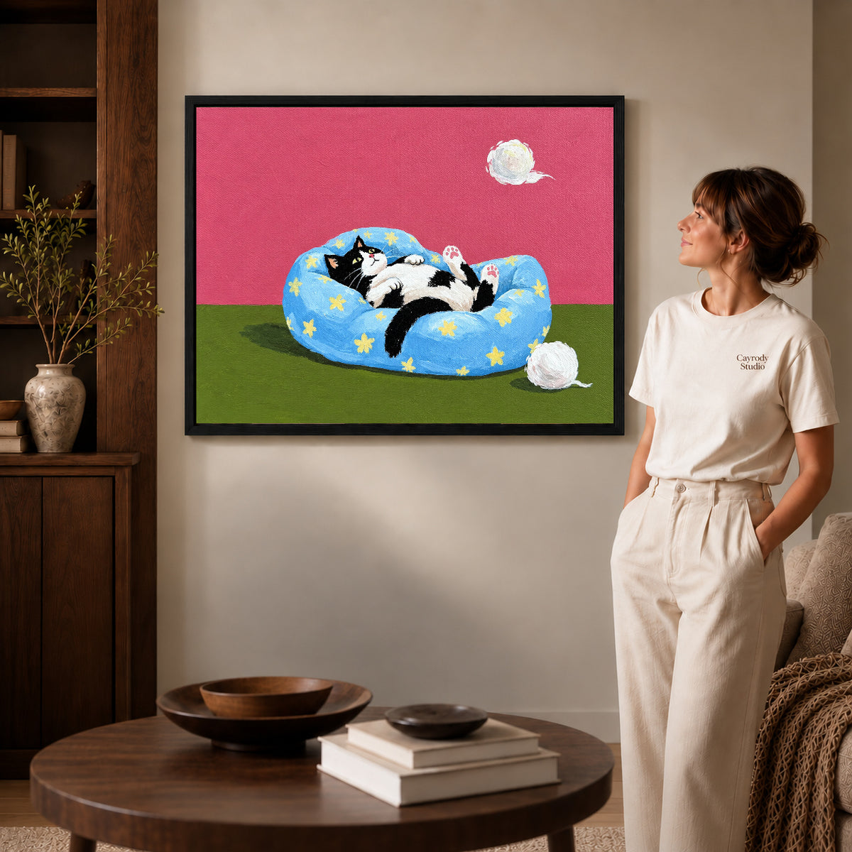 star bed cat canvas art in a black frame beside a woman and round wooden table.