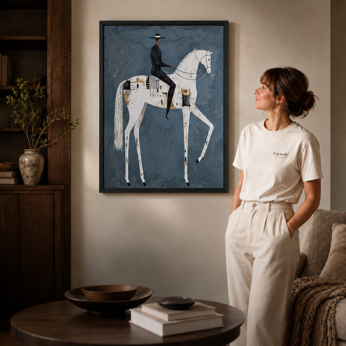 quiet equestrian poise canvas art in a black frame beside a woman and round wooden table.