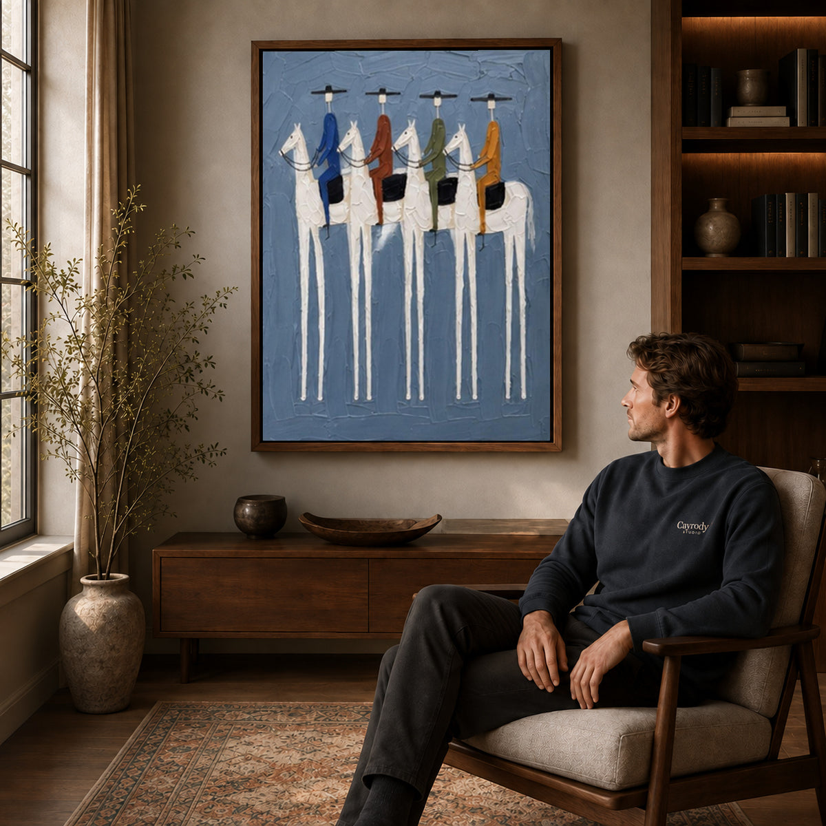 four riders together canvas art in a walnut frame above a console beside a seated man.