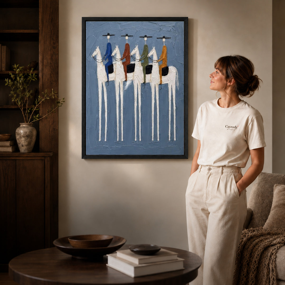 four riders together canvas art in a black frame beside a woman and round wooden table.