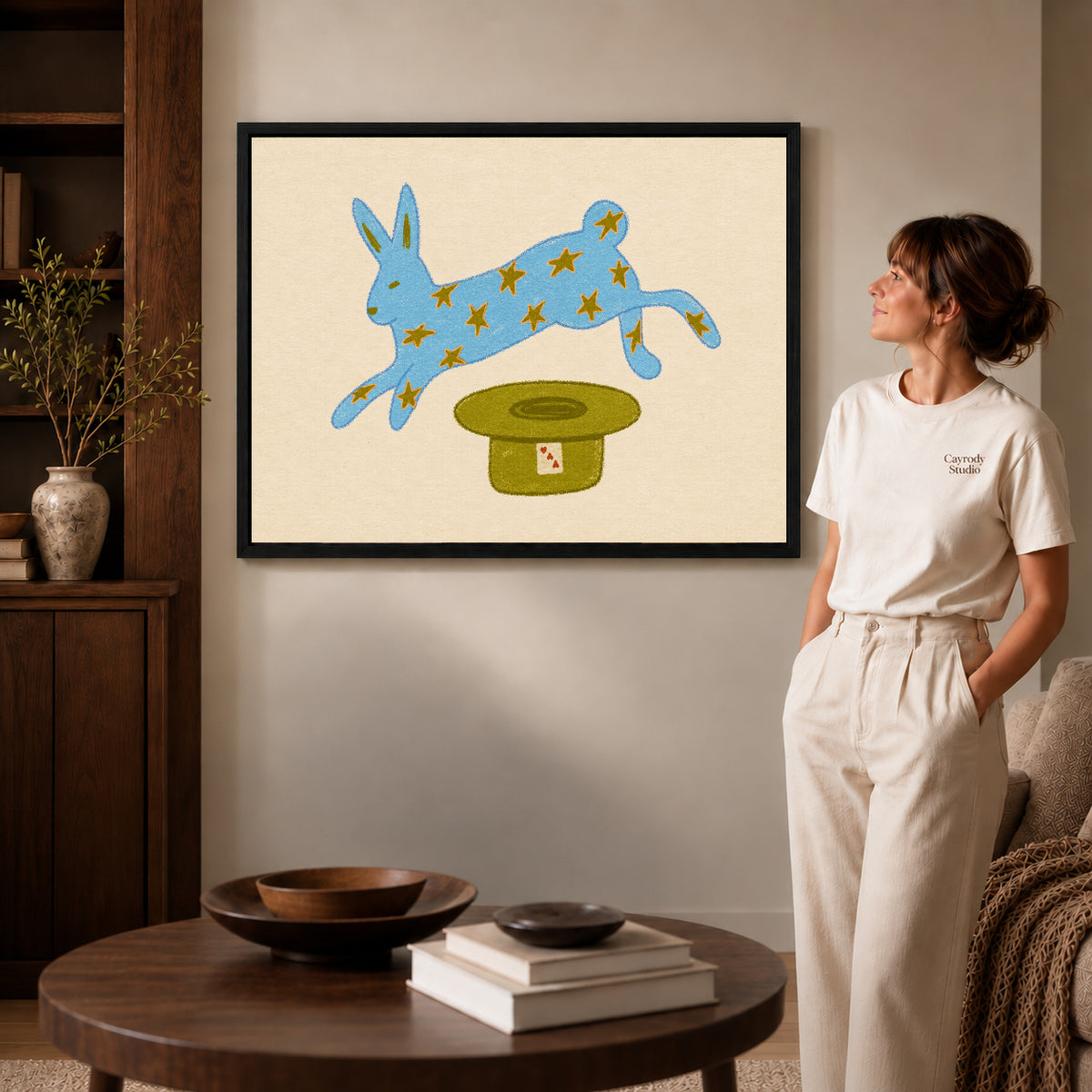 star rabbit magic canvas art in a black frame beside a woman and round wooden table.