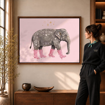 pink boot elephant canvas art in a walnut frame beside a standing woman and wooden console.