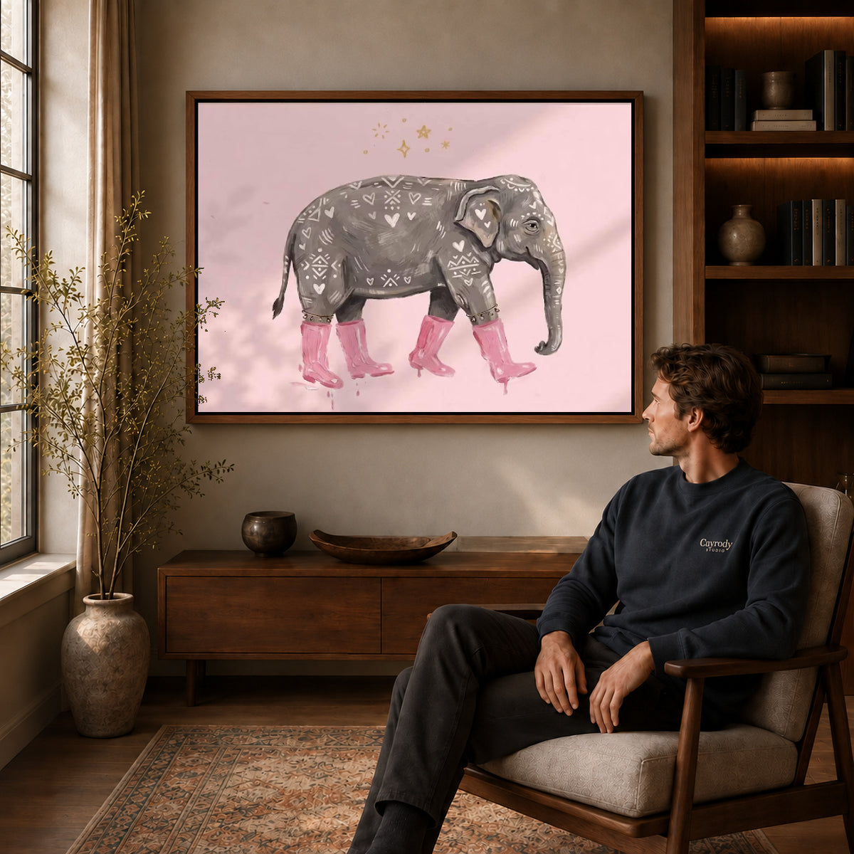pink boot elephant canvas art in a walnut frame above a console beside a seated man.