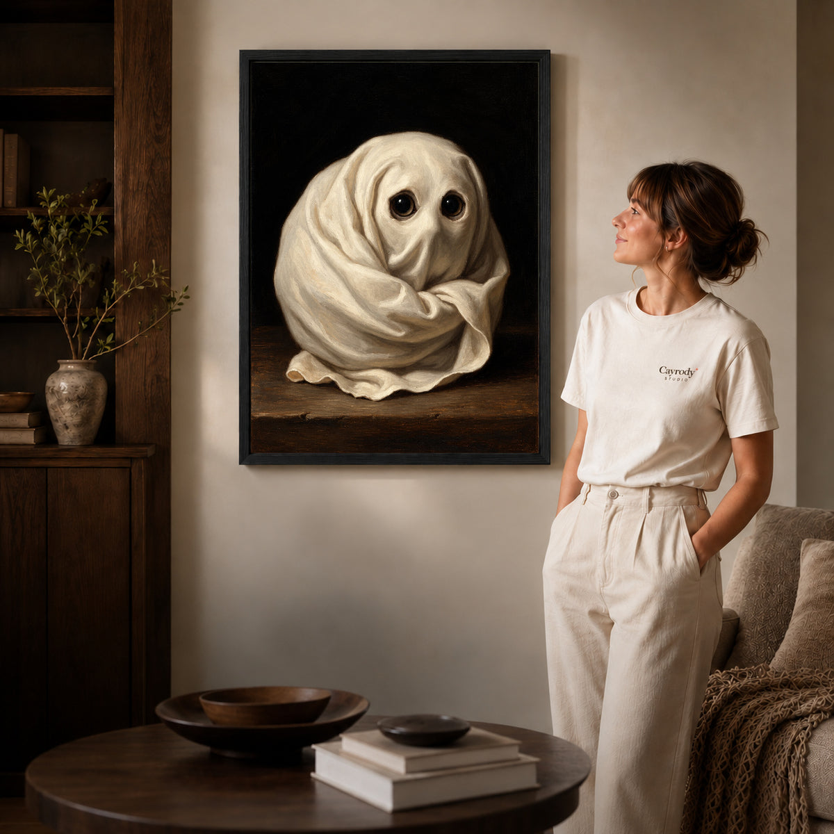 little ghost eyes canvas art in a black frame beside a woman and round wooden table.