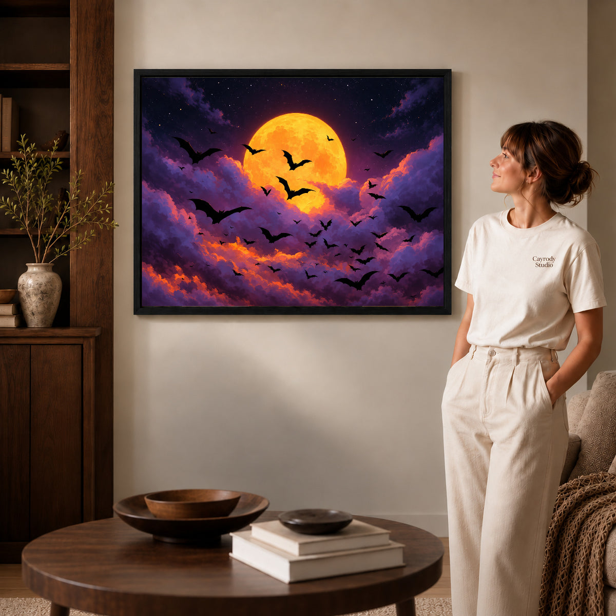 golden moon bats canvas art in a black frame beside a woman and round wooden table.