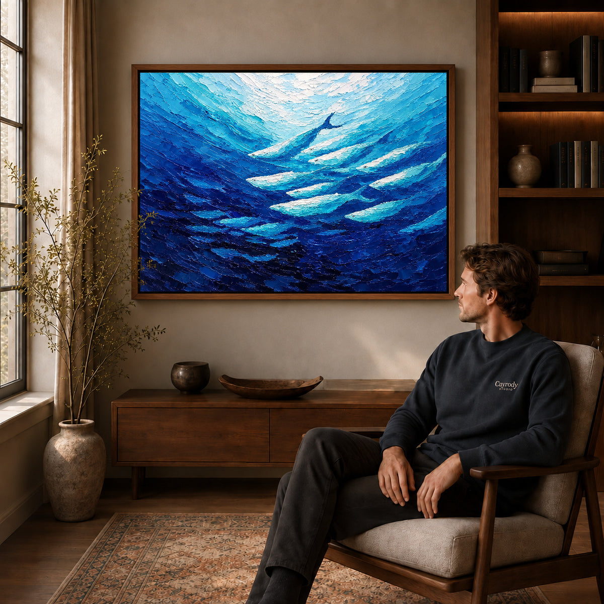 cobalt fish current canvas art in a walnut frame above a console beside a seated man.