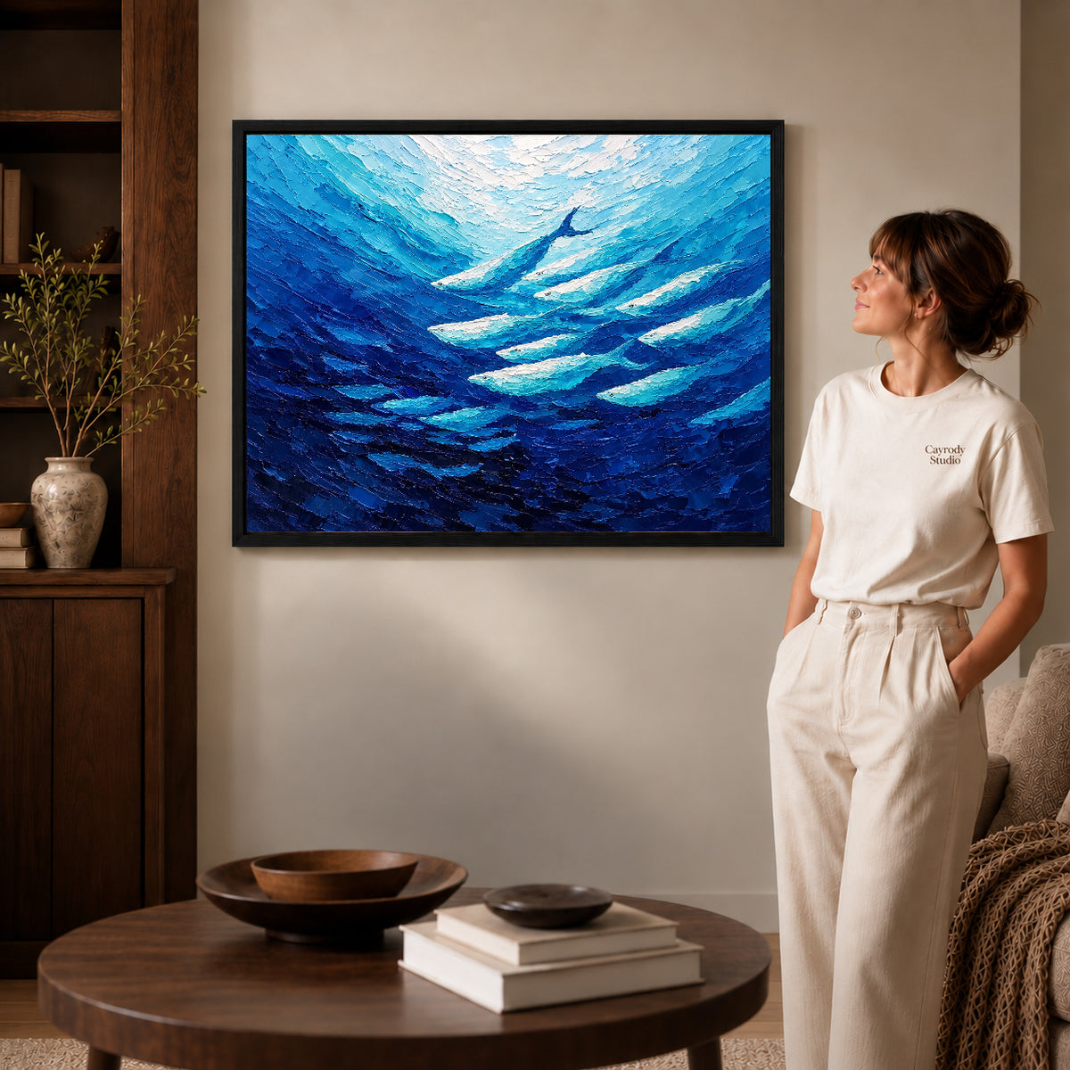 cobalt fish current canvas art in a black frame beside a woman and round wooden table.