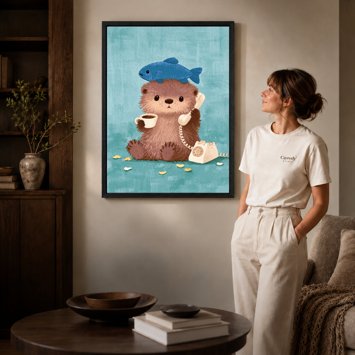 otter coffee call canvas art in a black frame beside a woman and round wooden table.