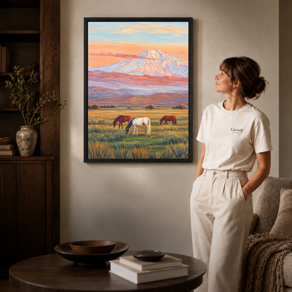 pastel mountain horses canvas art in a black frame beside a woman and round wooden table.