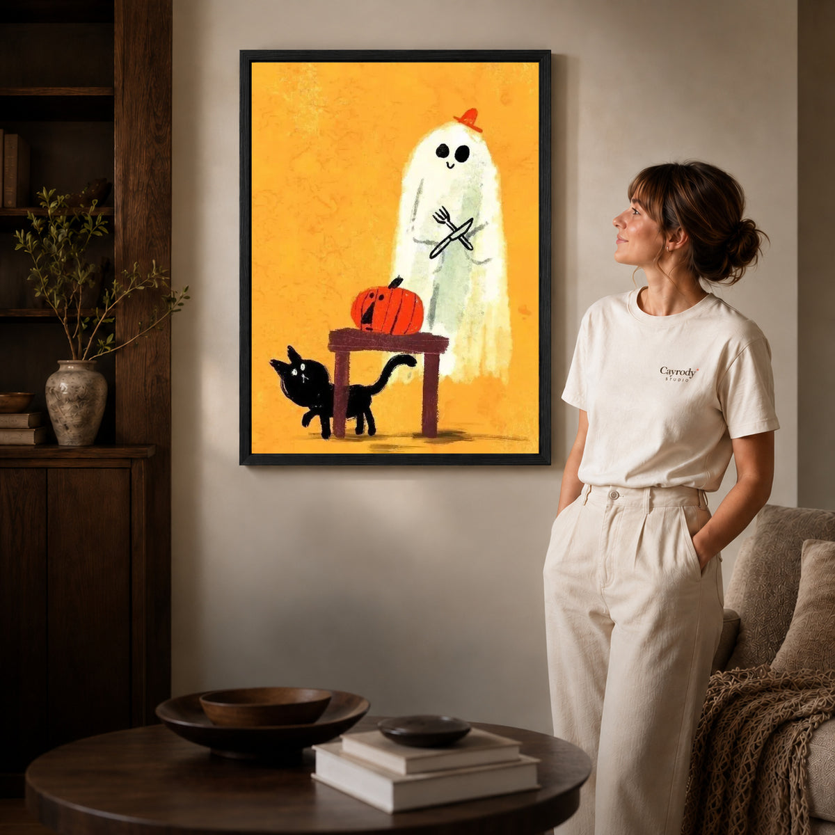 ghost dinner surprise canvas art in a black frame beside a woman and round wooden table.