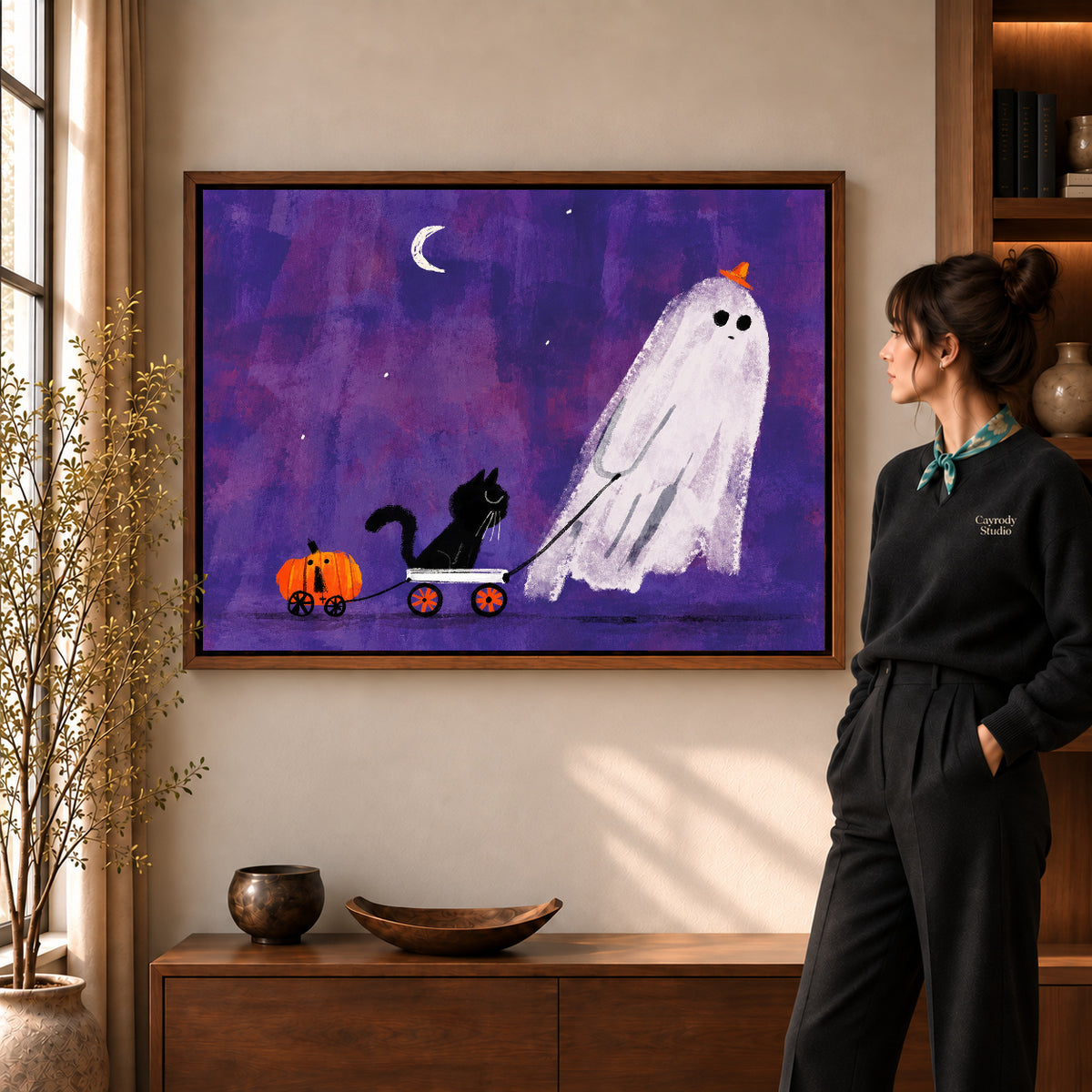 ghost wagon outing canvas art in a walnut frame beside a standing woman and wooden console.