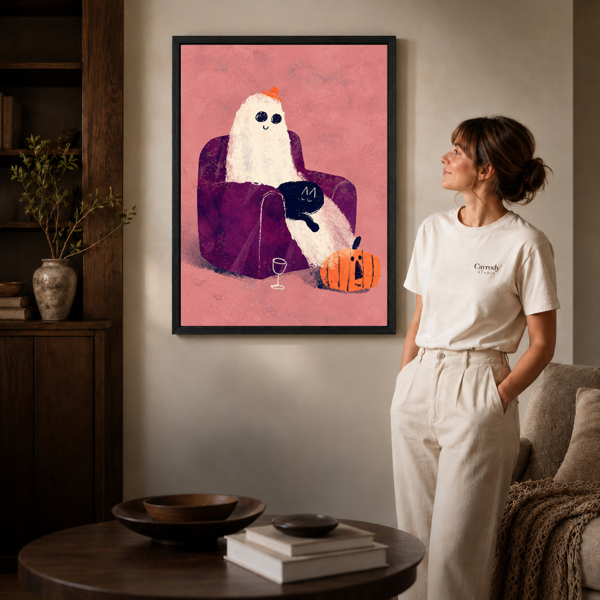 ghost armchair evening canvas art in a black frame beside a woman and round wooden table.