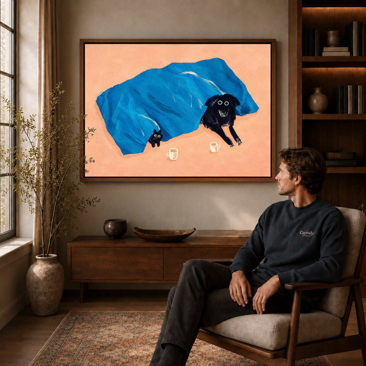 cozy blanket companions canvas art in a walnut frame above a console beside a seated man.