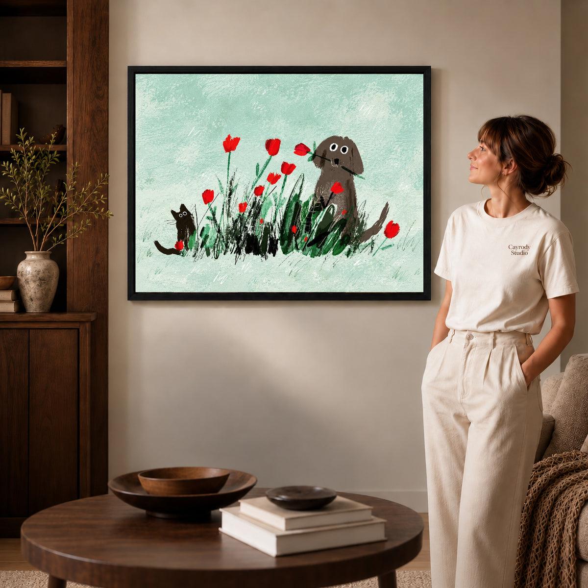 dog cat tulip garden canvas art in a black frame beside a woman and round wooden table.