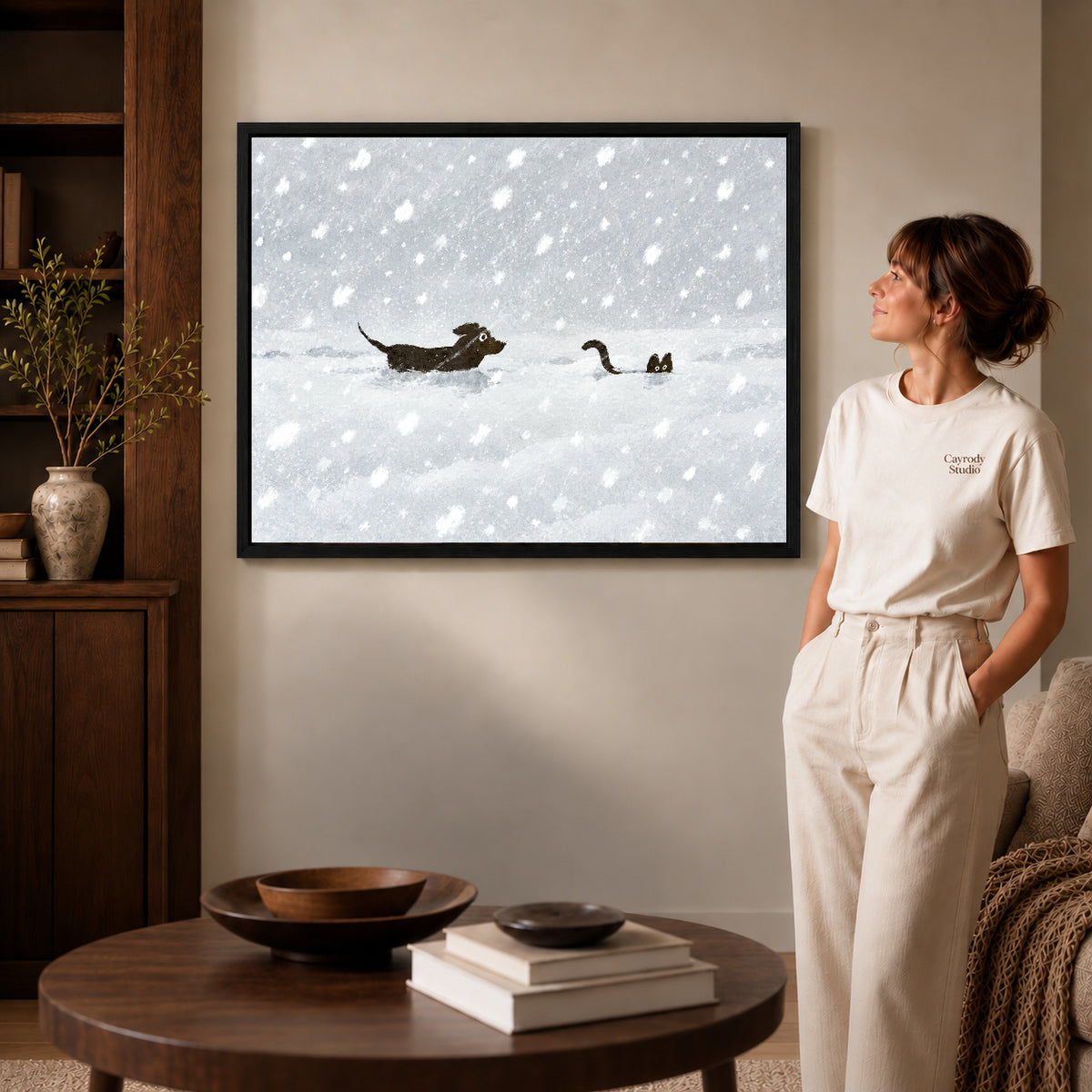 snow chase companions canvas art in a black frame beside a woman and round wooden table.