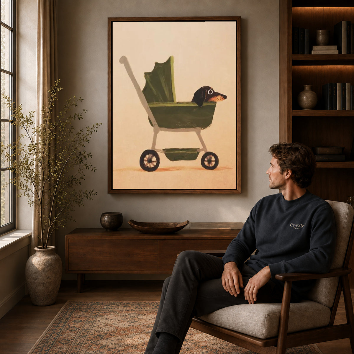 dachshund pram ride canvas art in a walnut frame above a console beside a seated man.