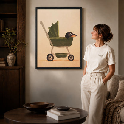 dachshund pram ride canvas art in a black frame beside a woman and round wooden table.