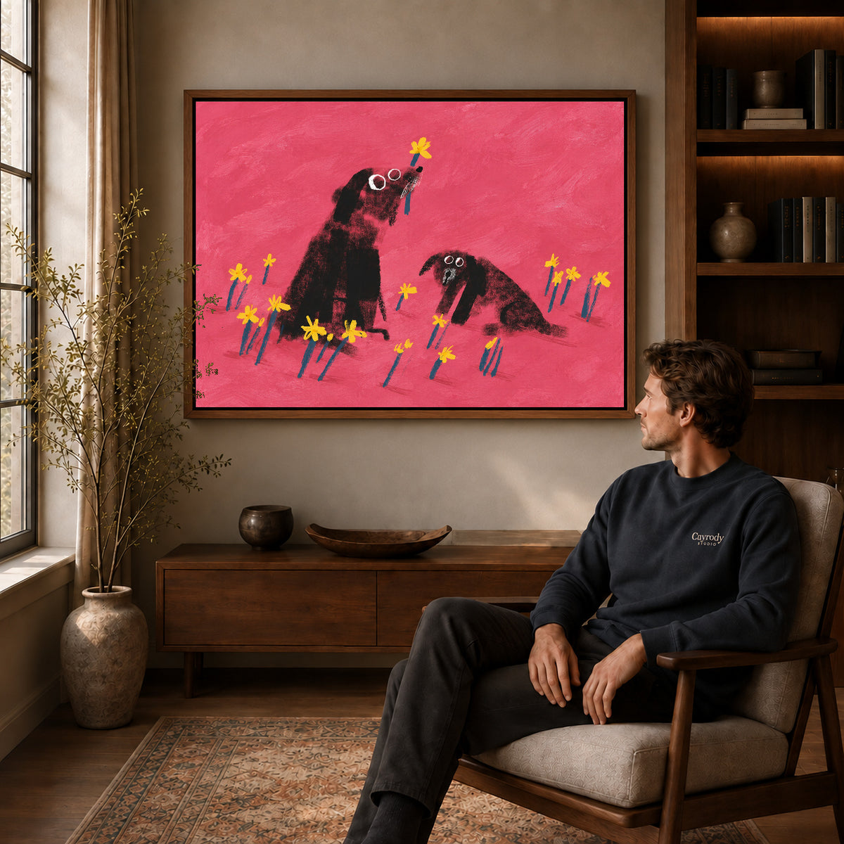 dogs among daffodils canvas art in a walnut frame above a console beside a seated man.