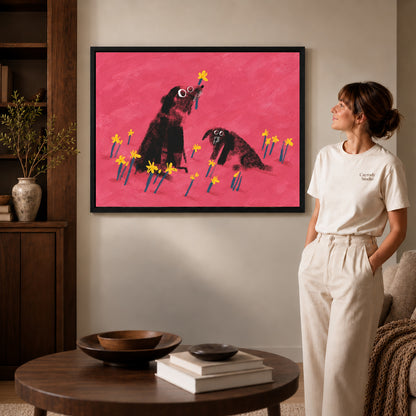 dogs among daffodils canvas art in a black frame beside a woman and round wooden table.