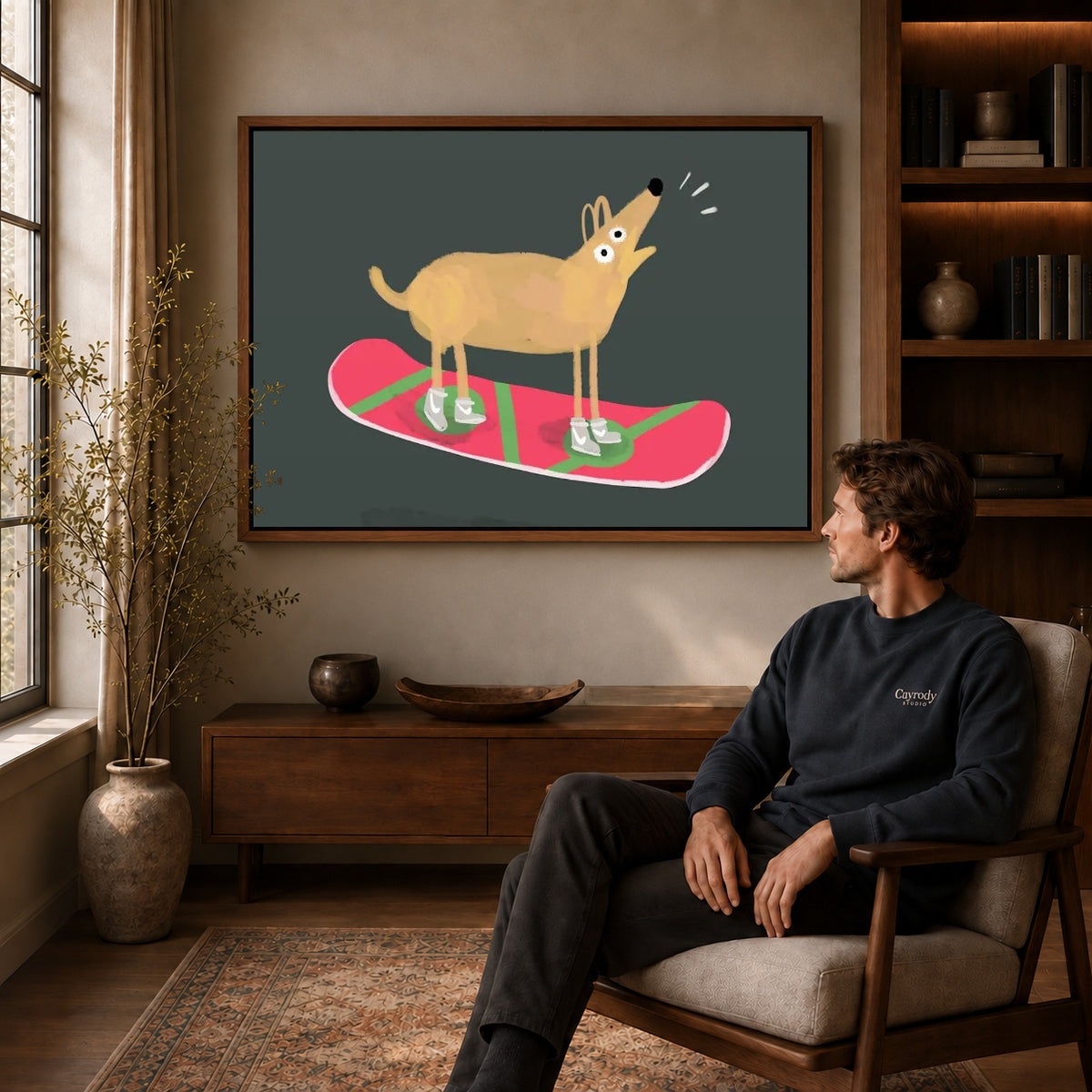 snowboard dog adventure canvas art in a walnut frame above a console beside a seated man.