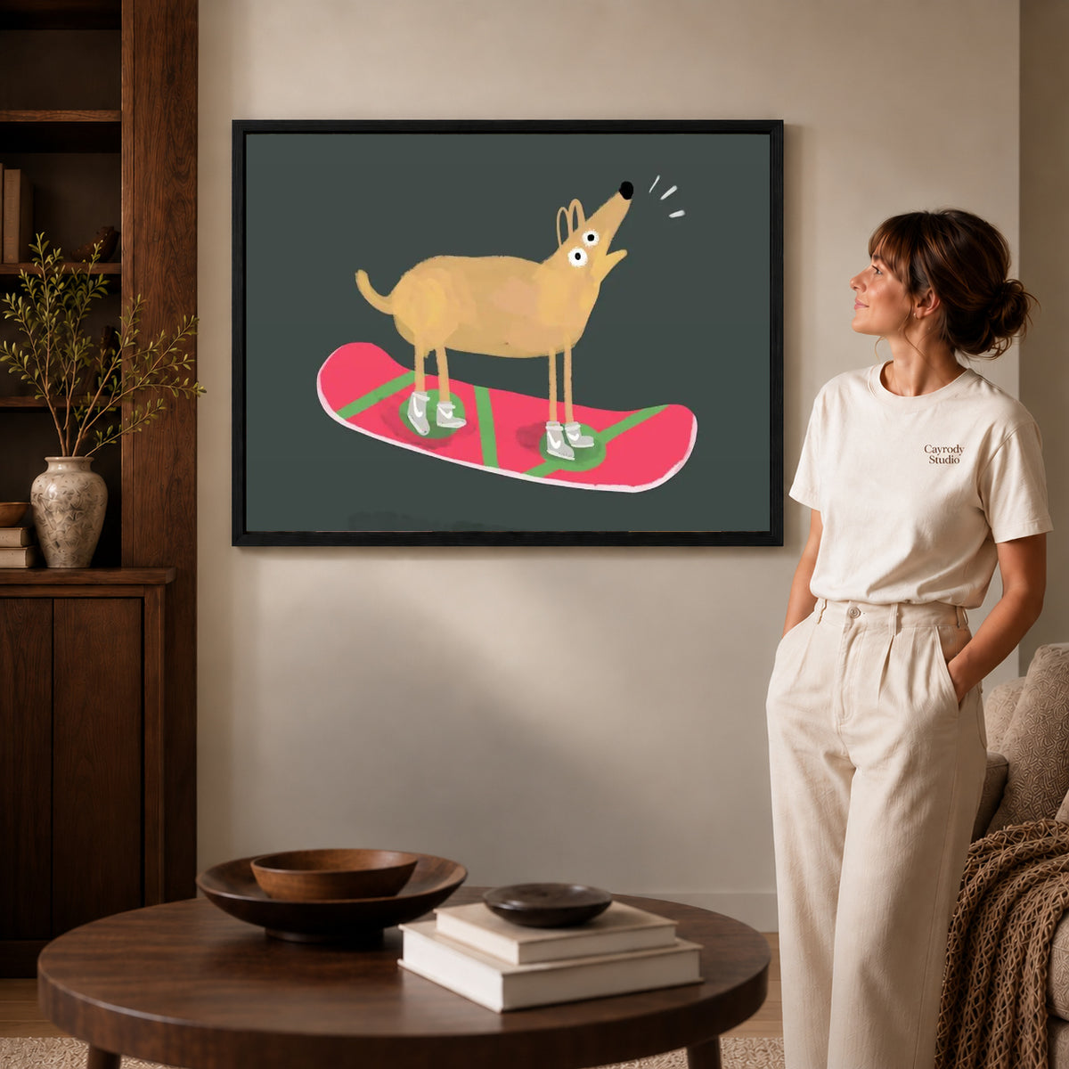 snowboard dog adventure canvas art in a black frame beside a woman and round wooden table.