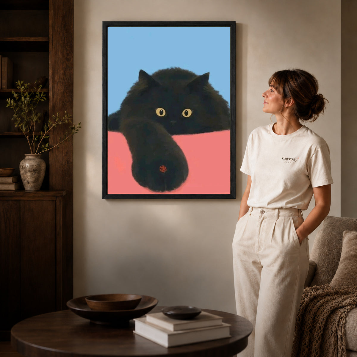ladybug paw pause canvas art in a black frame beside a woman and round wooden table.