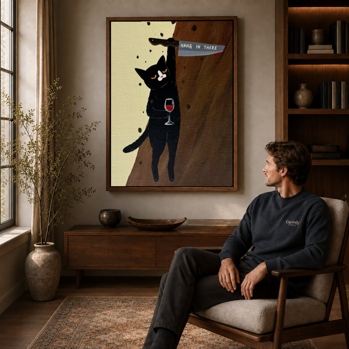 hang in there cat canvas art in a walnut frame above a console beside a seated man.