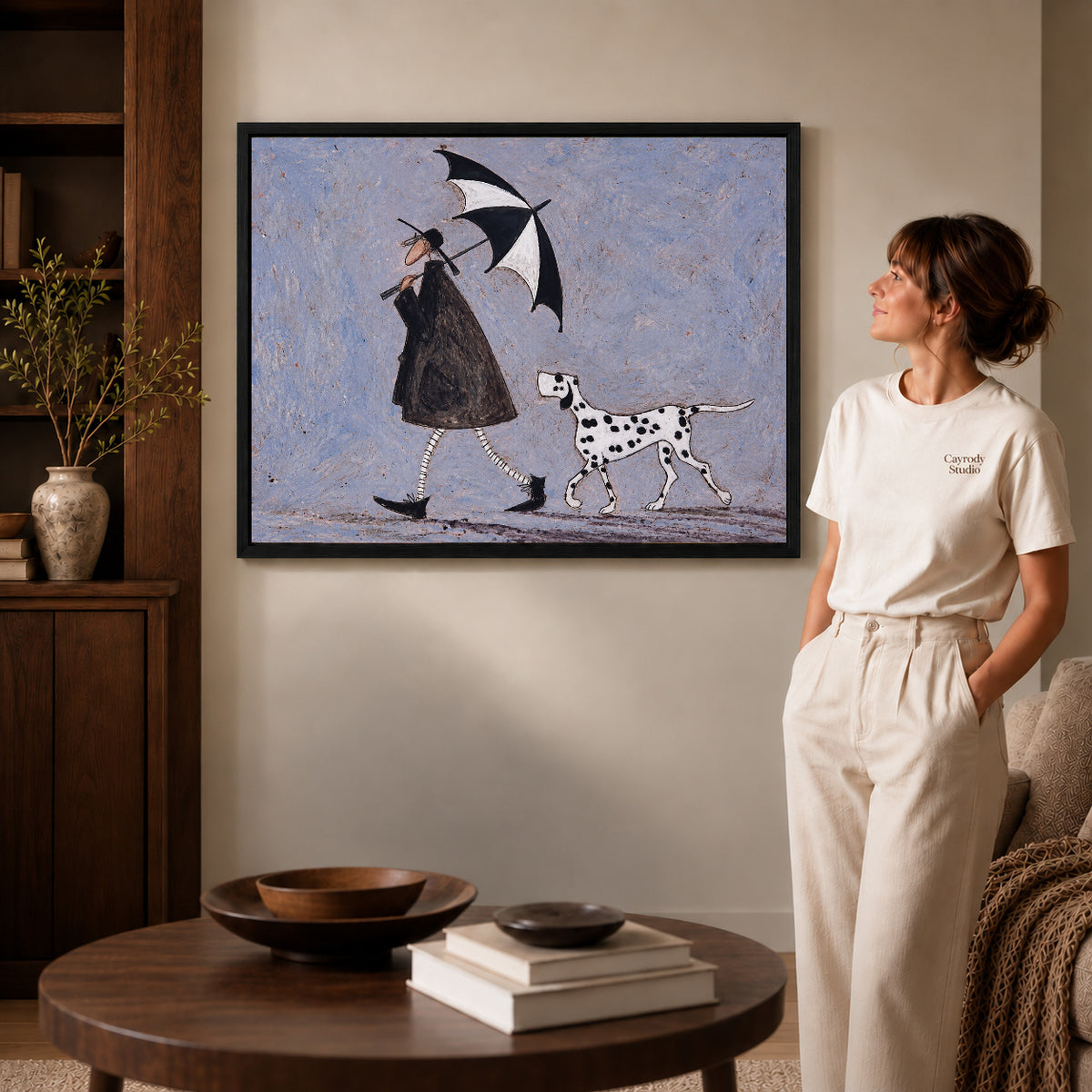 umbrella walk companions canvas art in a black frame beside a woman and round wooden table.