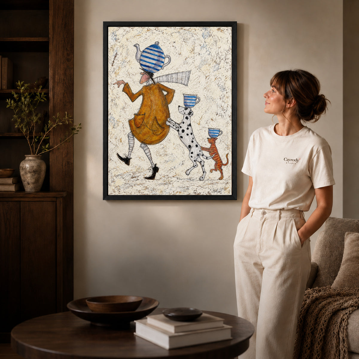 teacup walking parade canvas art in a black frame beside a woman and round wooden table.