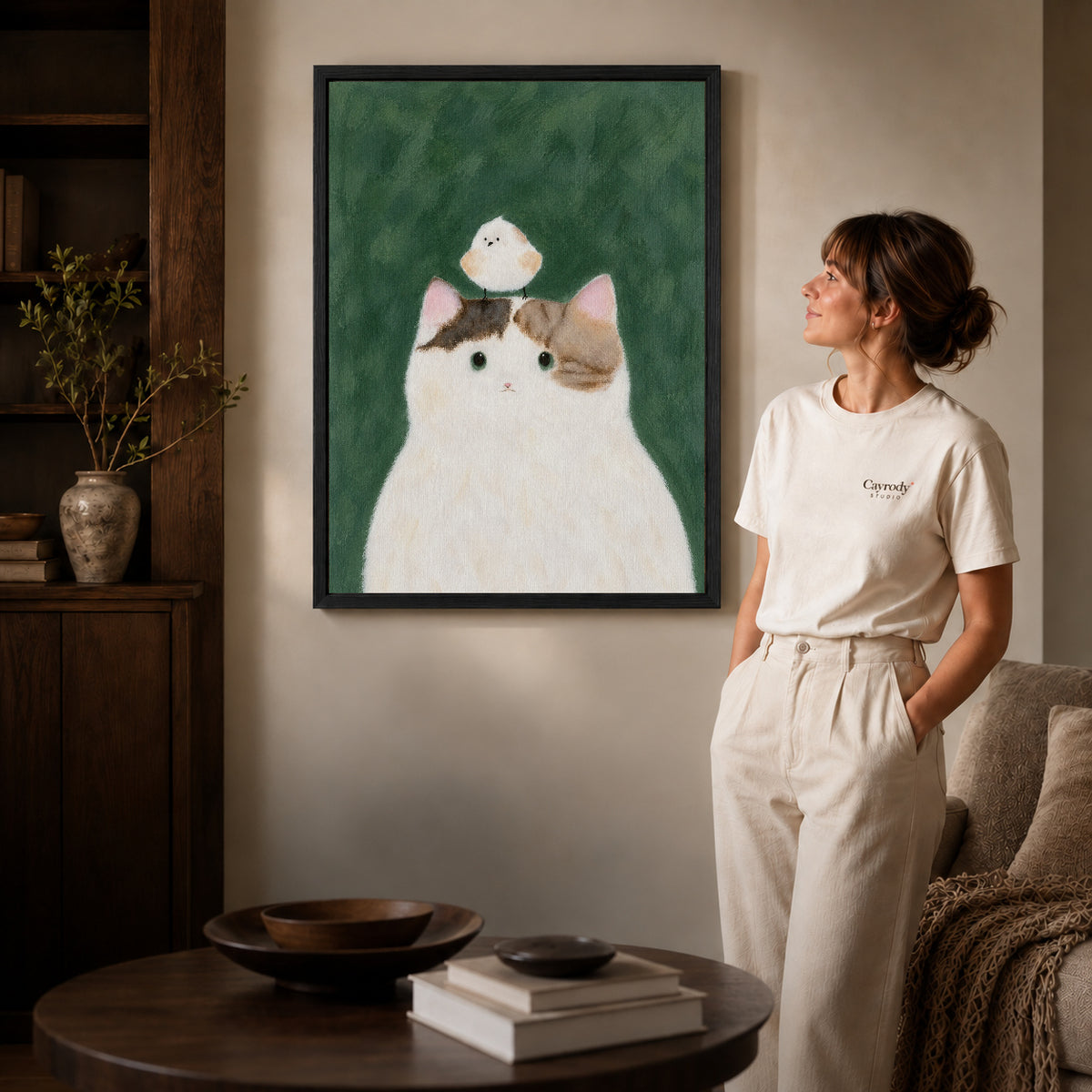 cat bird gentle friendship canvas art in a black frame beside a woman and round wooden table.