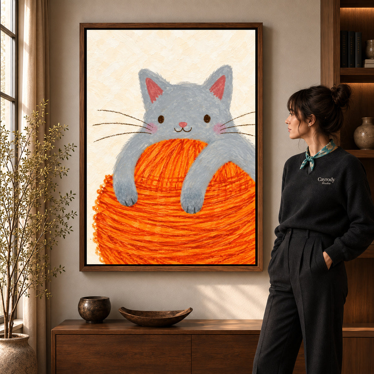 kitten yarn hug canvas art in a walnut frame beside a standing woman and wooden console.