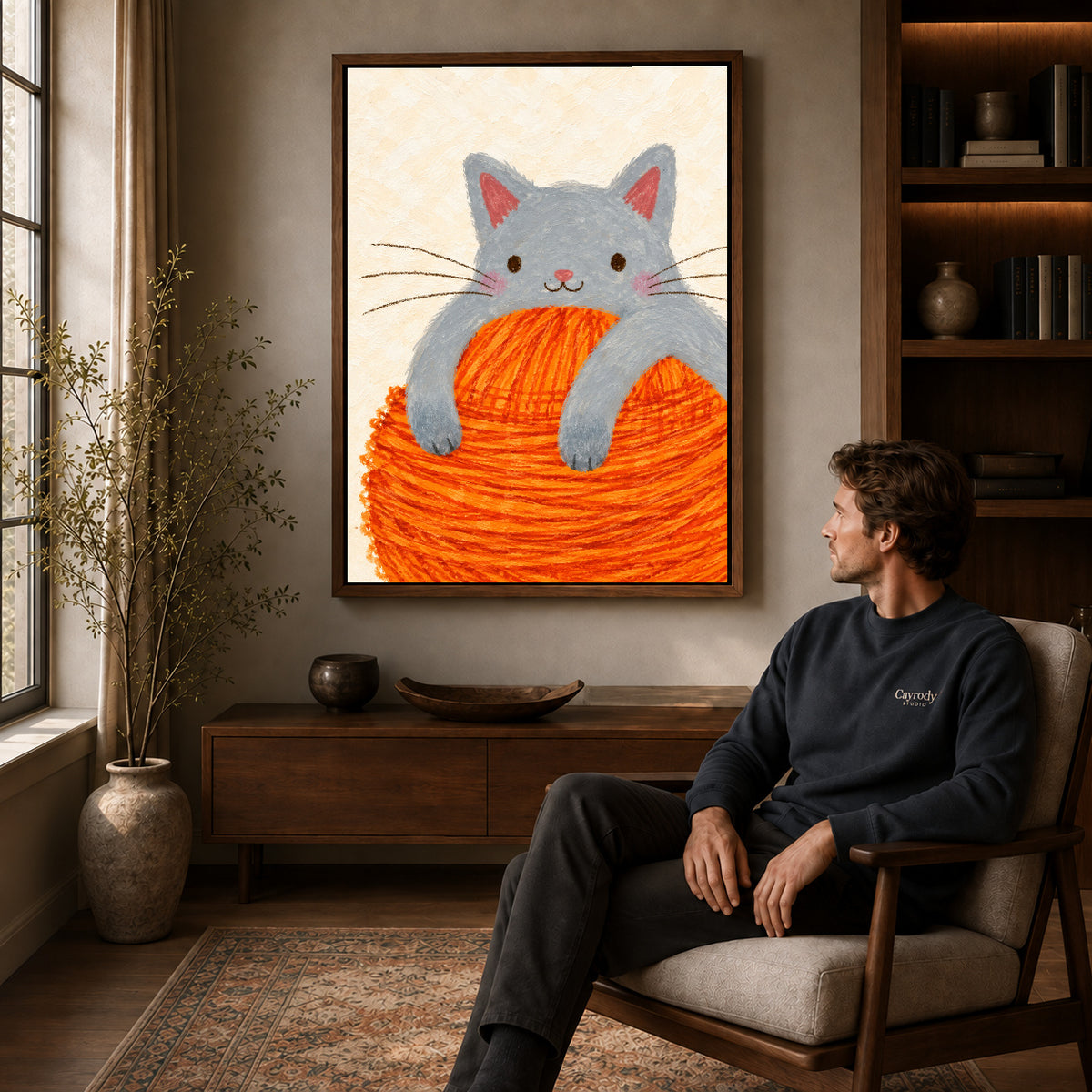kitten yarn hug canvas art in a walnut frame above a console beside a seated man.