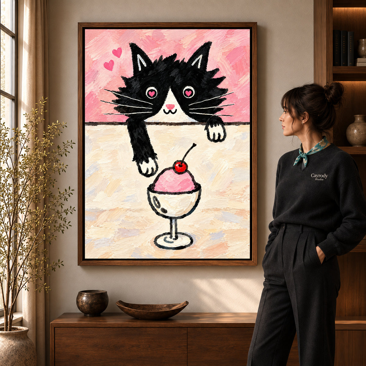 ice cream cat canvas art in a walnut frame beside a standing woman and wooden console.