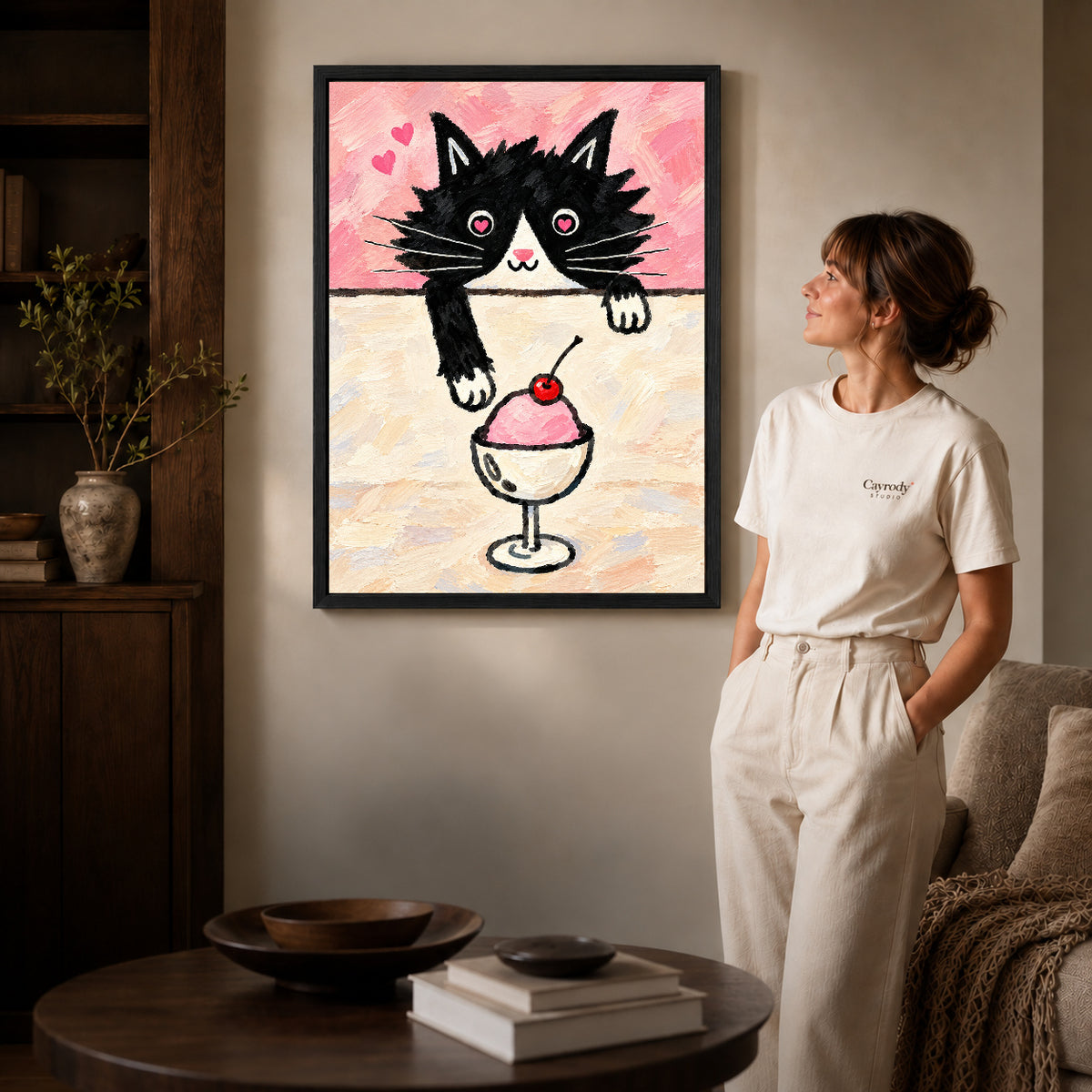 ice cream cat canvas art in a black frame beside a woman and round wooden table.