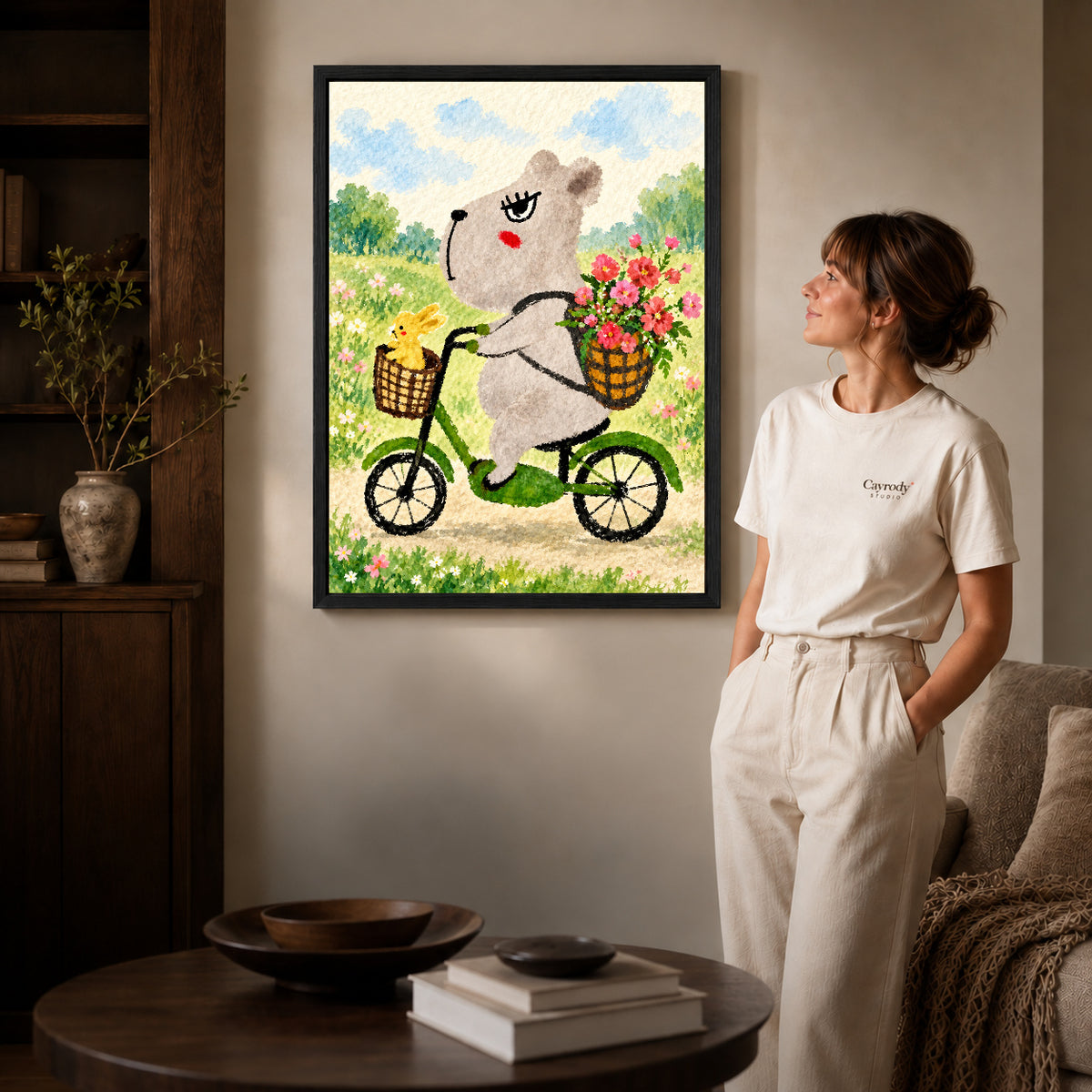 capybara bicycle ride canvas art in a black frame beside a woman and round wooden table.