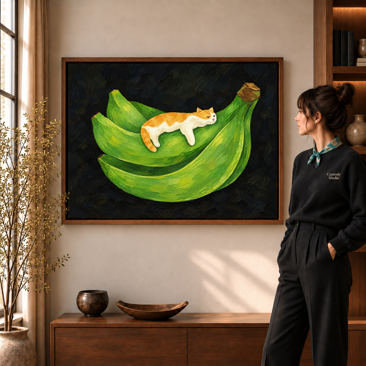 banana cat nap canvas art in a walnut frame beside a standing woman and wooden console.