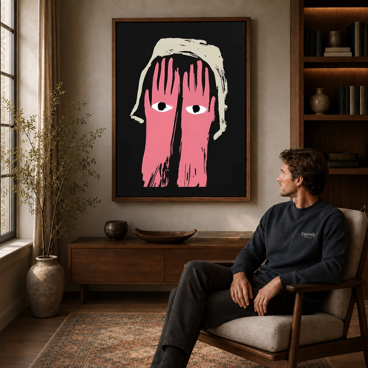 pink hands watch canvas art in a walnut frame above a console beside a seated man.
