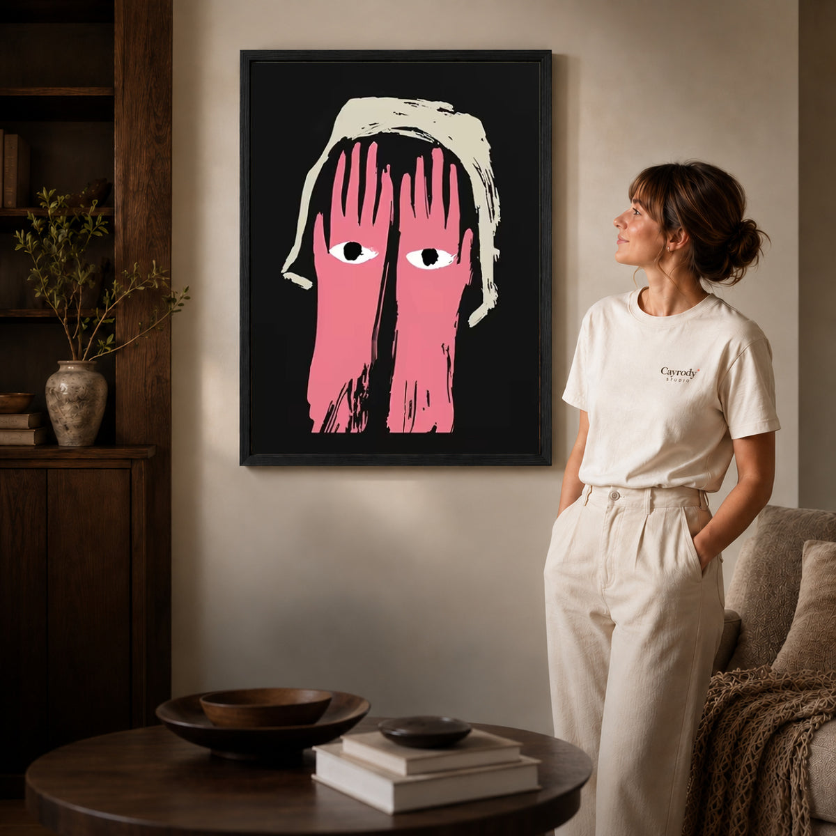 pink hands watch canvas art in a black frame beside a woman and round wooden table.