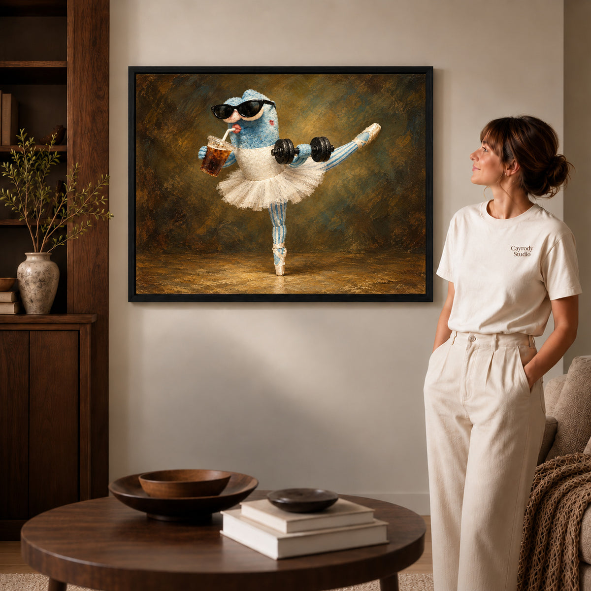 whimsical ballet balance canvas art in a black frame beside a woman and round wooden table.