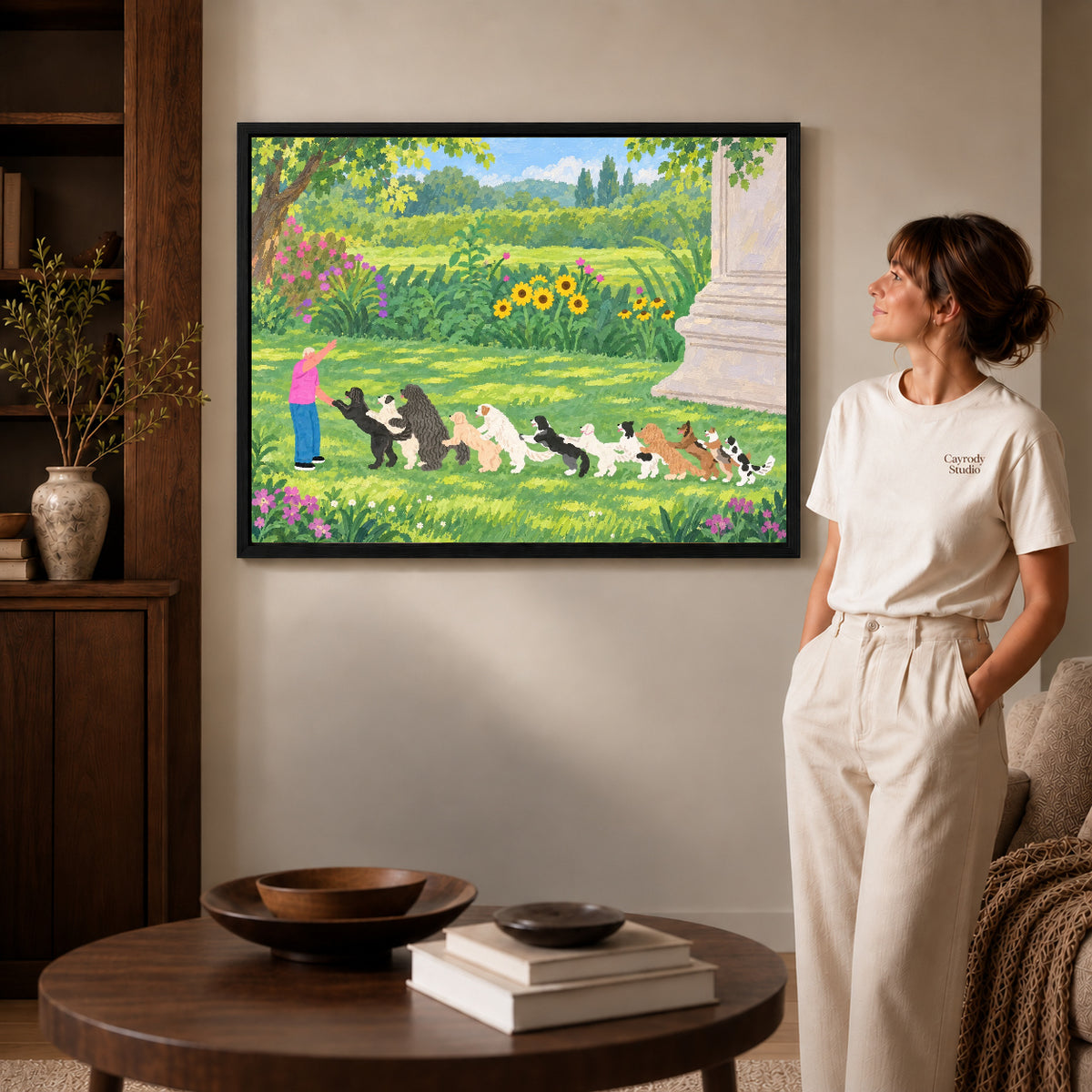 garden dog parade canvas art in a black frame beside a woman and round wooden table.