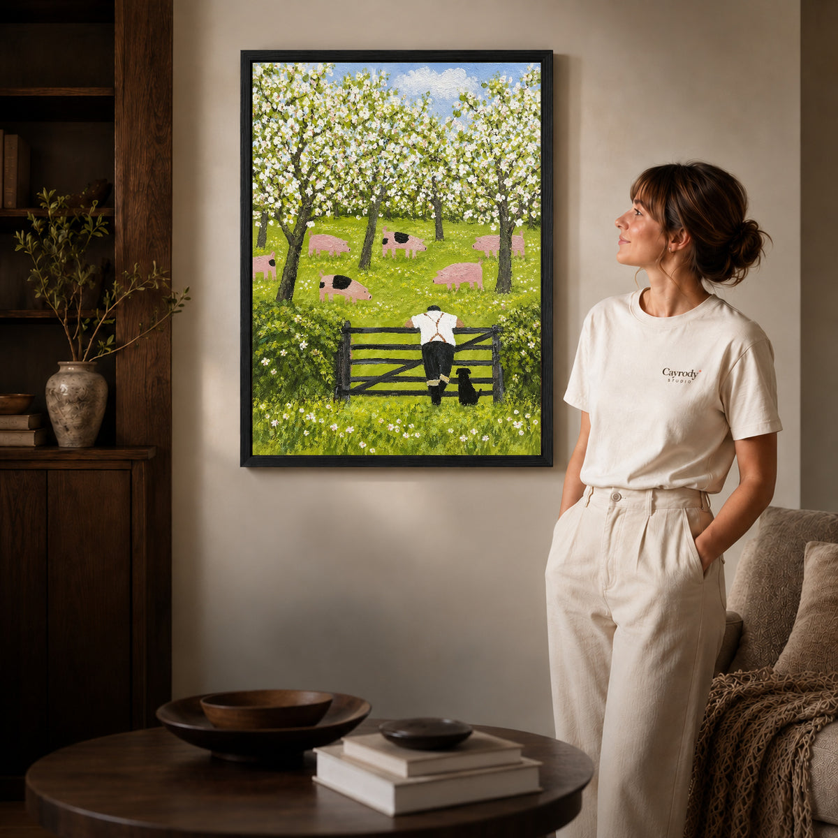 blossom orchard companions canvas art in a black frame beside a woman and round wooden table.
