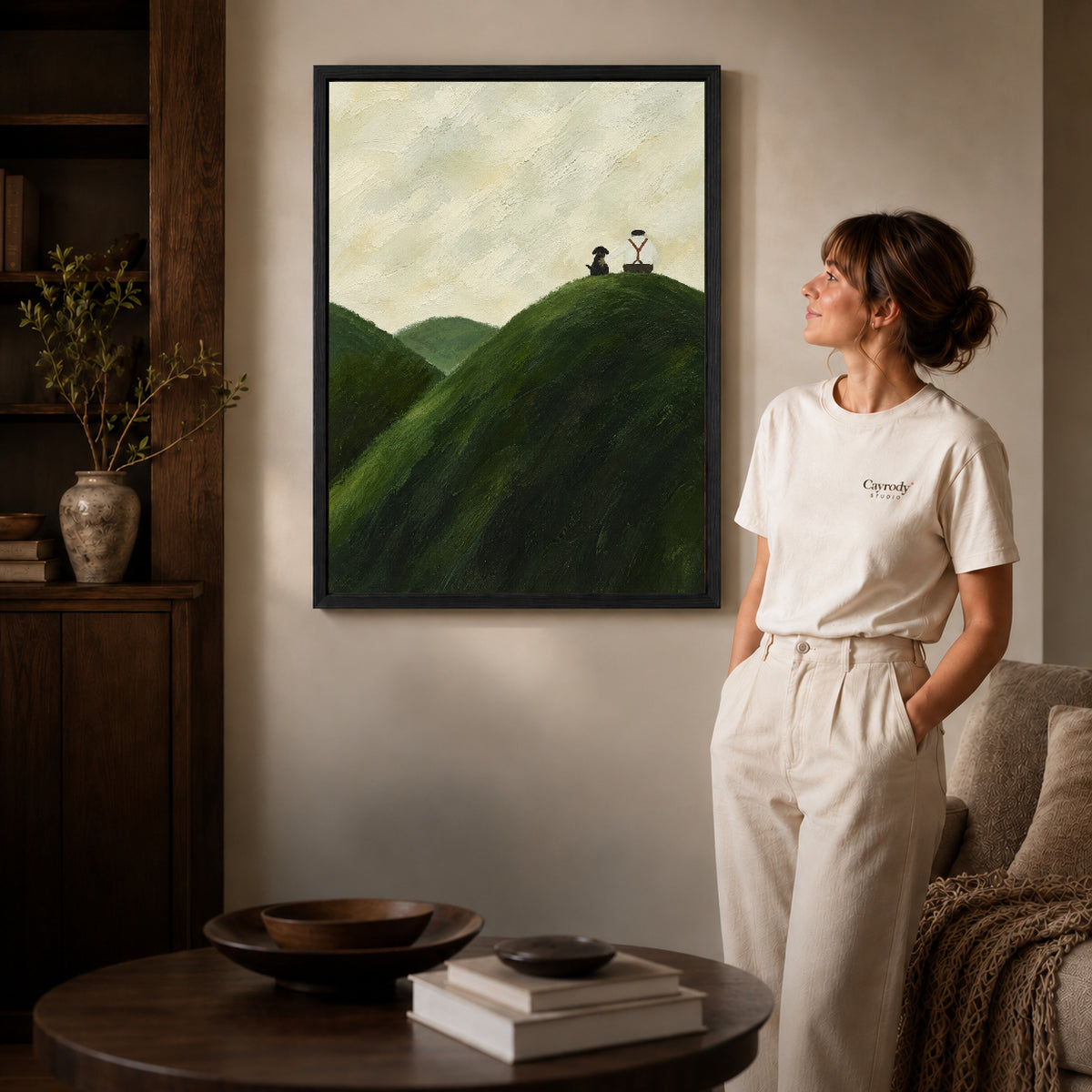hilltop quiet company canvas art in a black frame beside a woman and round wooden table.