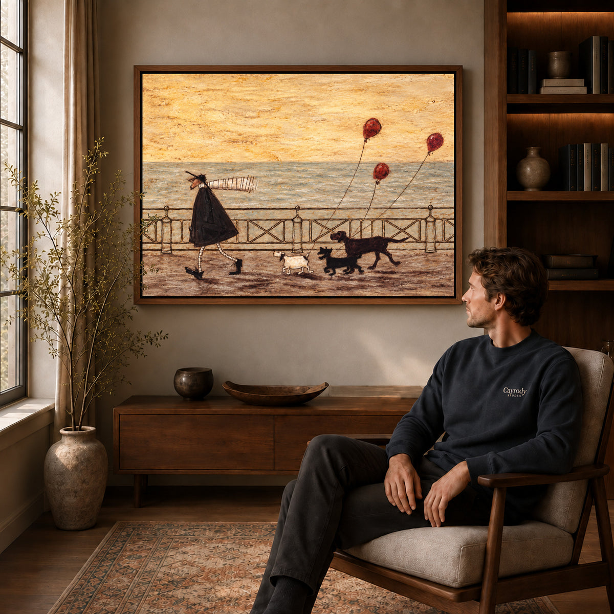 seaside dog walk canvas art in a walnut frame above a console beside a seated man.