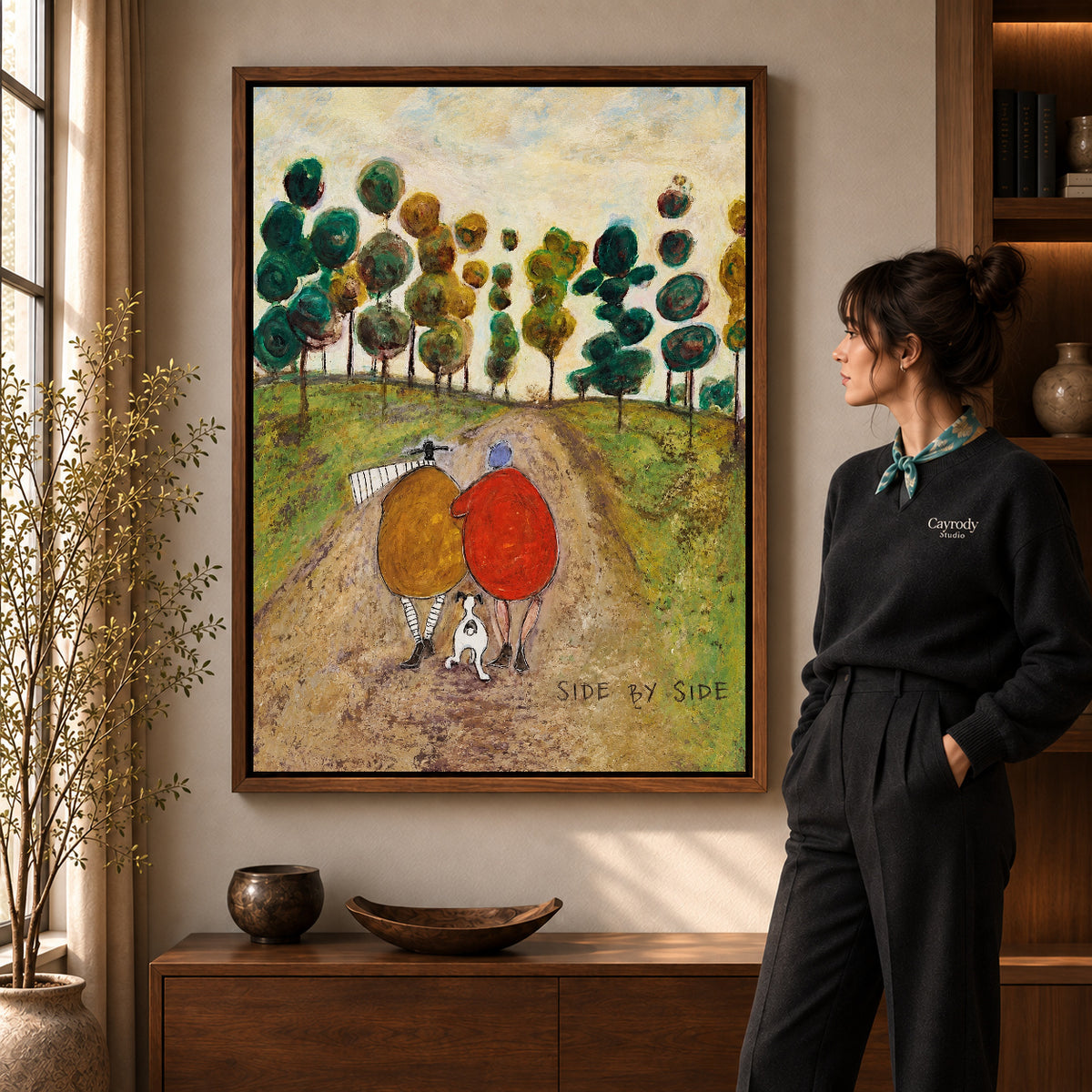 side by side canvas art in a walnut frame beside a standing woman and wooden console.