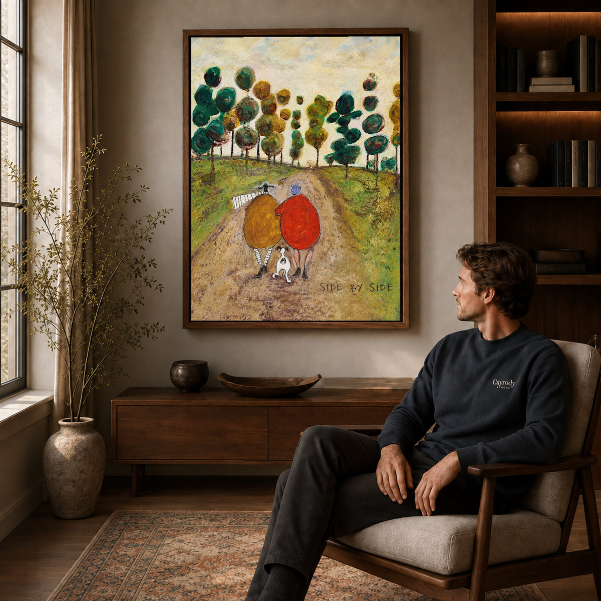 side by side canvas art in a walnut frame above a console beside a seated man.