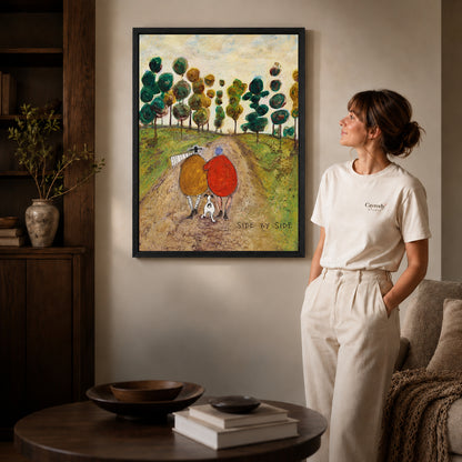 side by side canvas art in a black frame beside a woman and round wooden table.