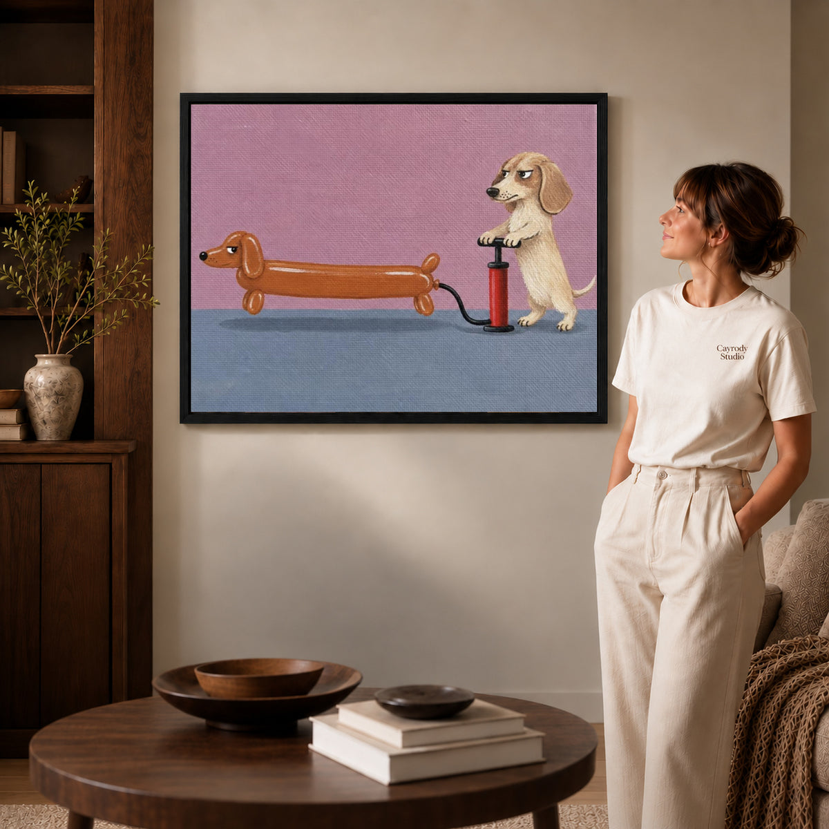 Black framed dachshund balloon canvas art displayed beside a woman in a warm neutral living room.