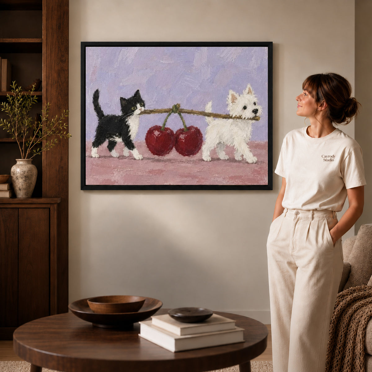Black framed cherry carrying pets canvas art displayed beside a woman in a warm neutral living room.